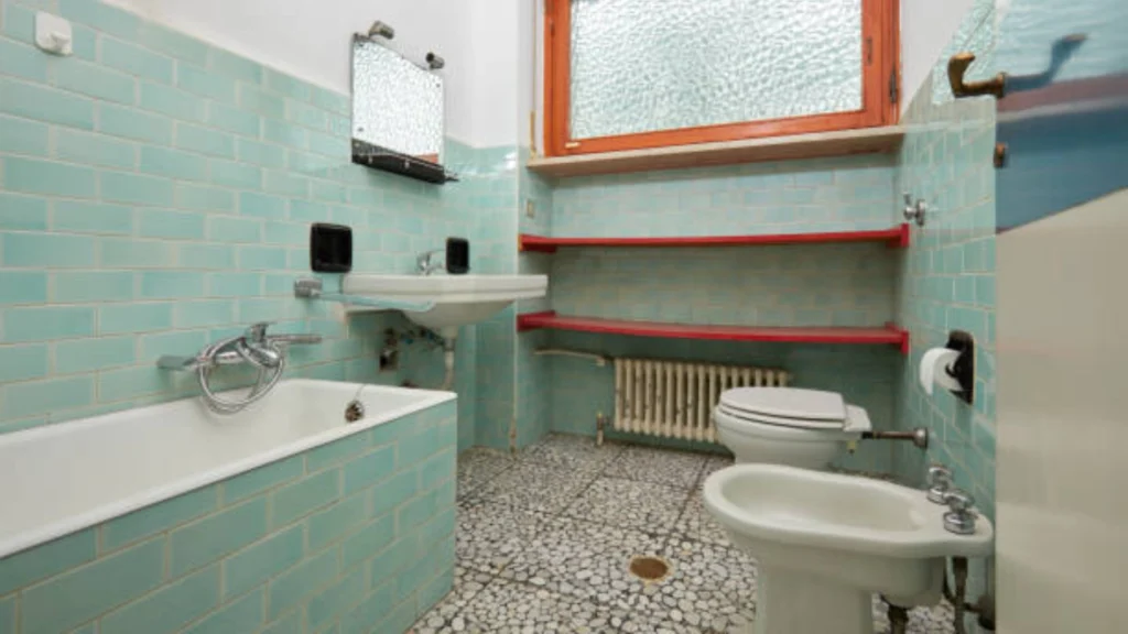 Retro bathroom with turquoise tiles, bathtub, bidet, red shelves, and window. -bathroom remodel companies