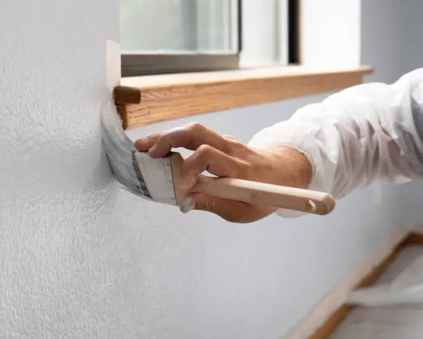 Hand carefully paints interior wall trim, demonstrating difference between interior and exterior paint.