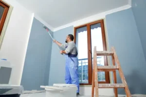 Painter rolls blue color on indoor walls, highlighting difference between interior and exterior paint.