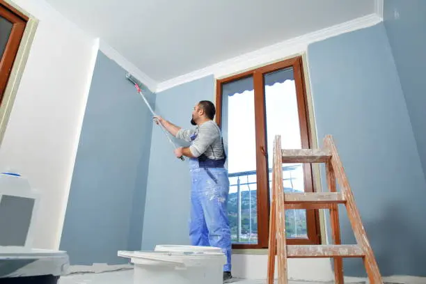Painter rolls blue color on indoor walls, highlighting difference between interior and exterior paint.