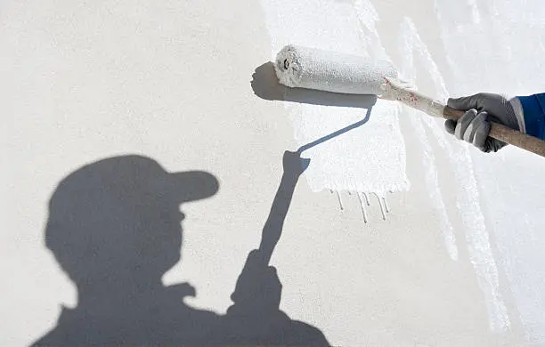 Worker applies outdoor wall paint, showing difference between interior and exterior paint.