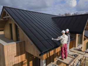 An image of two construction workers installing black metal roofing on a modern wooden accessory dwelling unit (ADU) under construction, illustrating ADU building processes in Seattle.